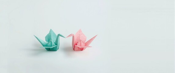 Obraz premium Origami paper cranes made from recycled paper in pastel teal and pink, positioned to face each other against a white background