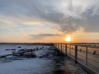 Obraz premium Winter sunset over the snow-covered Ihaste bridge and frozen Emajõgi River, Tartu, Tartumaa, Estonia, January 2021