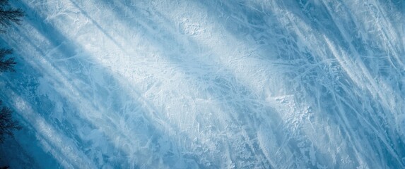 Bird's-eye view of a calm frozen lake dotted with gentle shadows from trees, depicting a serene winter landscape