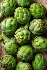 Fototapeta premium Fresh green artichokes arranged on rustic brown paper background with natural light and textured leaf details