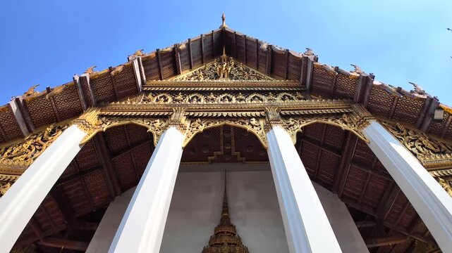 A low-angle view of the ornate golden pediment and white columns of a temple building at Bangkok's Grand Palace complex.