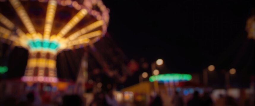 Abstract blurred picture of nighttime amusement park ride, featuring light, happiness, children, and entertainment background