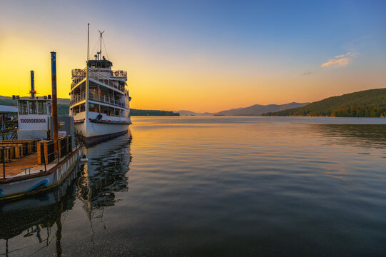Lake George, New York, USA - June 11, 2025 : Tour boat docked on Lake George at sunset, with calm water and Adirondack Mountains in New York State.
