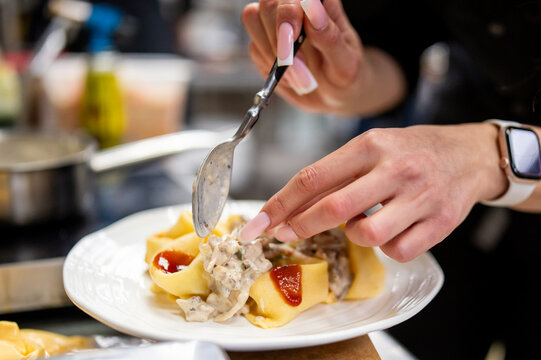 Close-up of a chef or home cook using a spoon to add creamy mushroom sauce to freshly prepared, large stuffed pasta on a white plate, highlighting the cooking process and appetizing presentation
