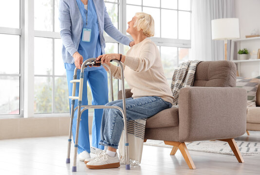 Nurse helping senior woman with walker to get up from armchair