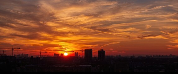 Fototapeta premium Sunset sky over Kyiv city with sun, clouds, and cranes