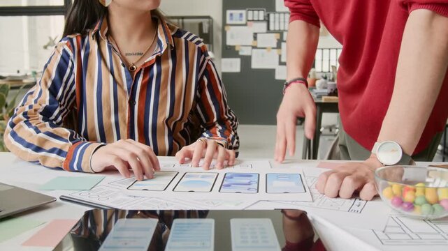 Medium shot of two unrecognizable young male and female mobile application designers discussing variants for wireframe mockup concepts, while collaborating together in startup office