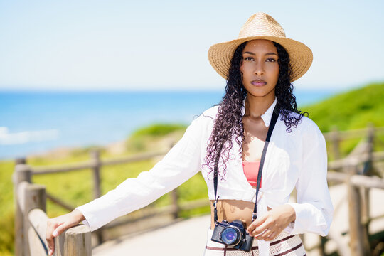 A Stylish Woman in a Trendy Straw Hat Capturing Cherished Moments by the Beautiful Ocean