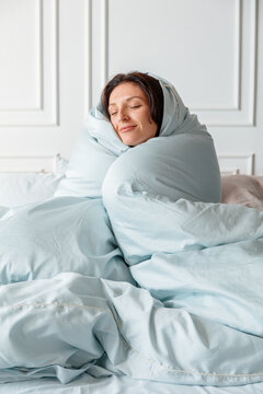 A person examines a bedding label that shows super king size and washing instructions while organizing their bedroom. The setting is warm and bright.
