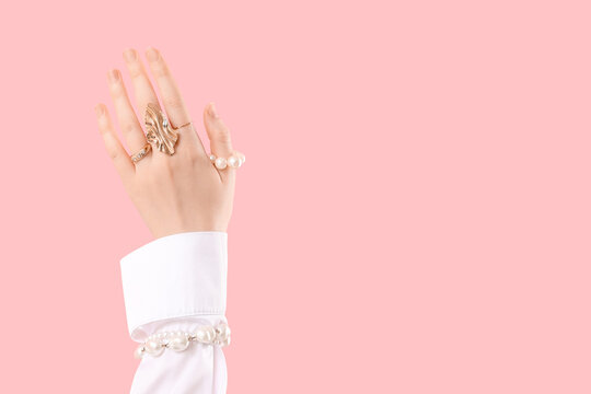 Female hand in beautiful pearl bracelets and rings on pink background