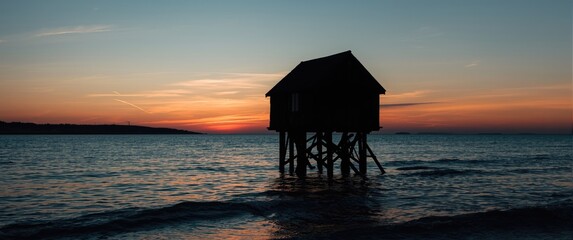 Saint Palais, France: Close-up of carrelet fishing during sunset, showcasing Poitou-Charentes' Charente Maritime area, wooden fishing huts, sea view, black and blue building details with orange hues