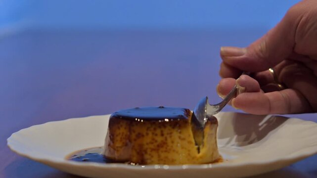 Hand eating a delicious cr&egrave;me caramel egg flan dessert with a spoon