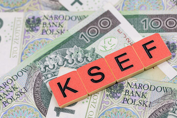 Blocks with the abbreviation KSEF, standing for National E-invoice System, are placed against a background of loosely spread Polish 100 PLN banknotes. The photo was taken under artificial lighting.