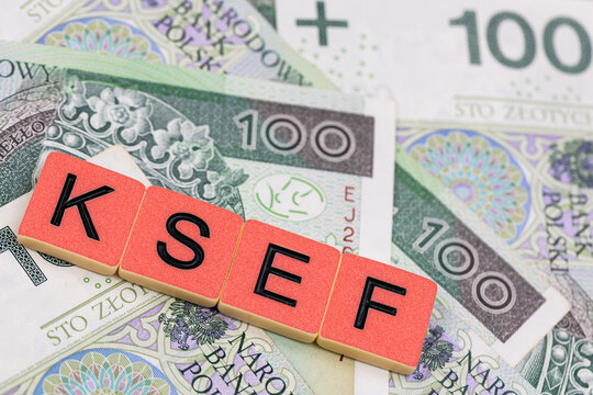 Blocks with the abbreviation KSEF, standing for National E-invoice System, are placed against a background of loosely spread Polish 100 PLN banknotes. The photo was taken under artificial lighting.