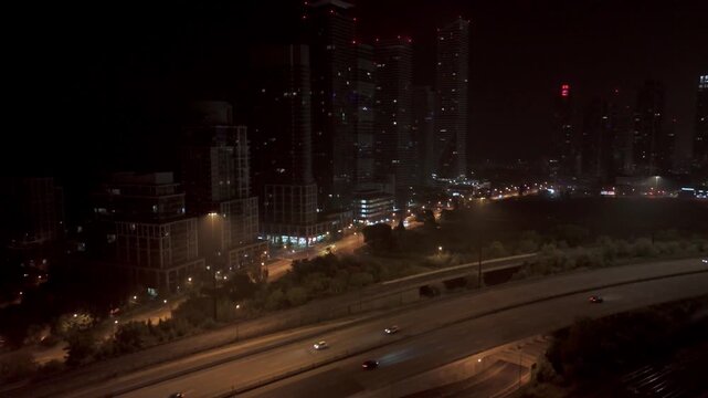 Cars Driving At Night On The Gardner Expressway By Condo Buildings At Parklawn In Toronto. Rising Drone Shot.