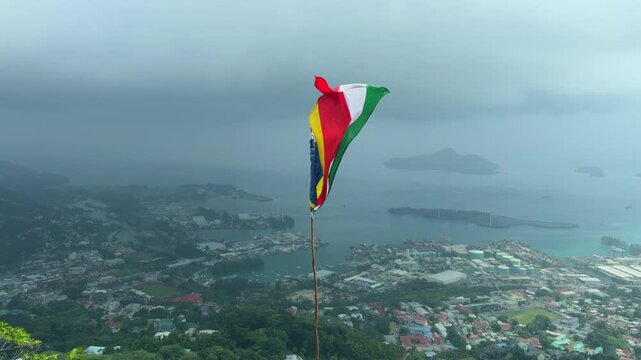 Seychelles flag floating above hill, beneath town Victoria and port area, Mahe, Seychelles 25fps 001.