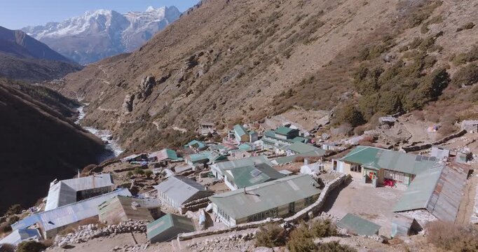 Over-the-roof drone shot of Shomare village on the Everest Base Camp route in Nepal. High-altitude settlement with the Dudh Koshi River flowing nearby and views toward Ama Dablam and Everest.