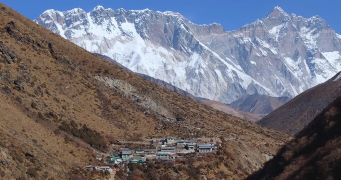 Smooth gliding aerial drone shot over Shomare village on the Everest Base Camp trek route in Nepal, revealing Mount Everest and Ama Dablam above a high-altitude residential settlement.