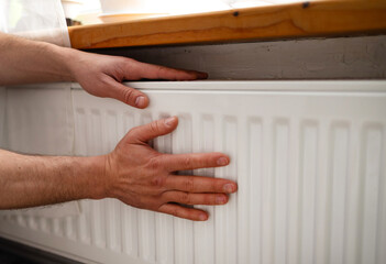Man is checking radiator is it heating. Man warming his hands on the radiator. Home central heating system. 