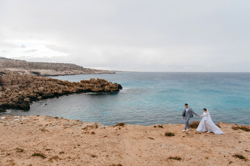 Newlyweds holding hands on a cliff overlooking the turquoise sea during a wedding photoshoot