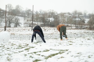 Two individuals collaborate on building a snowman in a snowy landscape. A winter scene unfolds...