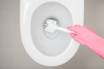 Woman hand in pink rubber protective glove holding brush and cleaning white toilet. Closeup. Top down view.