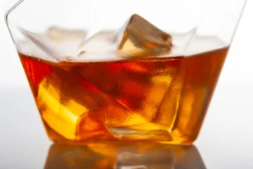 Cold whiskey cocktail with ice cubes in crystal glass, macro close up, amber alcohol drink texture, luxury bar beverage, refreshing drink concept, minimal studio background, selective focus. © Regina