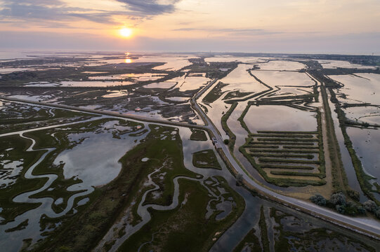 Aerial view of sun kissing the waters snaking through the wetlands, divided by roads and canals near Lio Piccolo, Veneto, Italy.