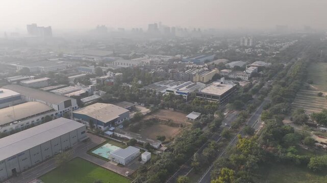 Aerial footage of industrial district under heavy haze, with warehouses, factories, and tree-lined plots blending into the smoggy urban skyline, pollution challenges in a growing Indian city