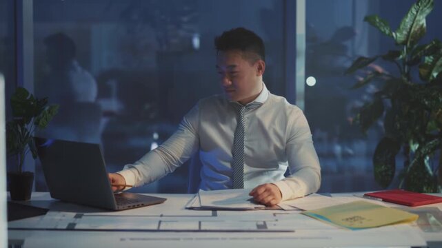 Successful architect reviewing blueprints confidently, Asian designer celebrating project milestone at night
