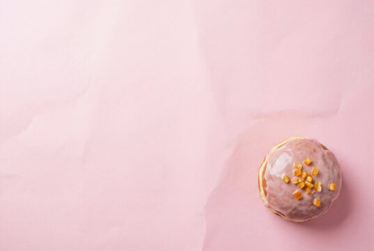 Traditional sweet glazed doughnut with candied orange peel on a pastel pink paper background offering large copy space for Fat Thursday celebration