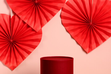 Red round podium for product display with paper hearts on pink background. Valentine's Day concept.