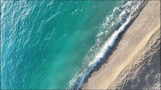 Dhermi, Albania - April 08, 2025: Aerial view of turquoise ocean waves gently lapping against a sandy beach, showcasing the serene coastal landscape in bright sunlight