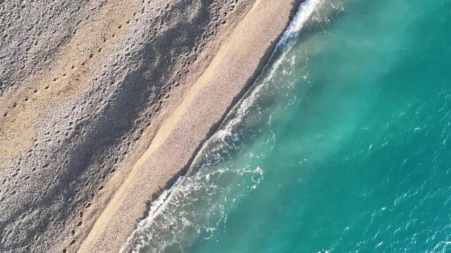 Dhermi, Albania - April 08, 2025: Aerial view of sandy beach with gentle waves lapping at the shore, showcasing the transition from land to water in a serene coastal setting