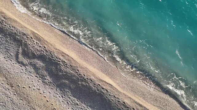 Dhermi, Albania - April 08, 2025: Aerial view of sandy beach with gentle waves lapping at the shore, showcasing distinct footprints leading towards the water's edge