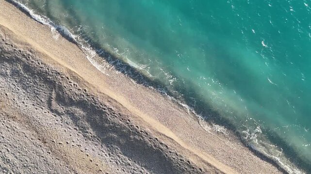 Dhermi, Albania - April 08, 2025: Aerial view of sandy beach shoreline with gentle waves lapping at the shore, showcasing the tranquil turquoise waters and pebbled sand