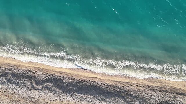 Dhermi, Albania - April 08, 2025: Aerial view of sandy beach with gentle waves lapping at the shore, turquoise water reflecting sunlight under a clear sky