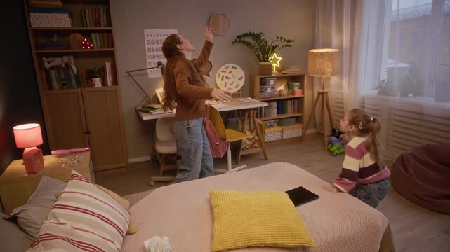 Caucasian mother and little daughter fooling around in room, playing with golden balloon