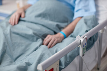 Middle aged Caucasian man lying in hospital bed with hand resting on blanket, wearing medical...