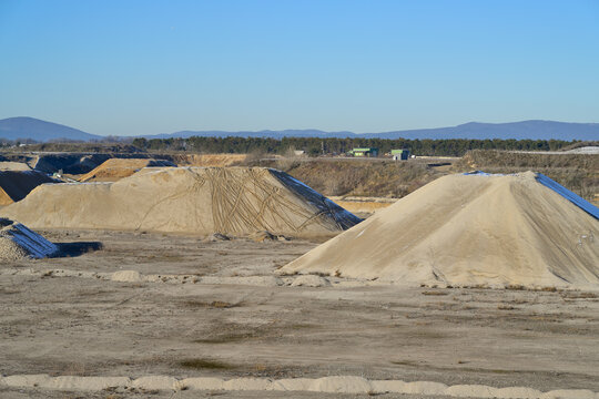 Sand and gravel quarry extracting building materials outdoor. Large sand and gravel piles dotting a mining site under blue sky.