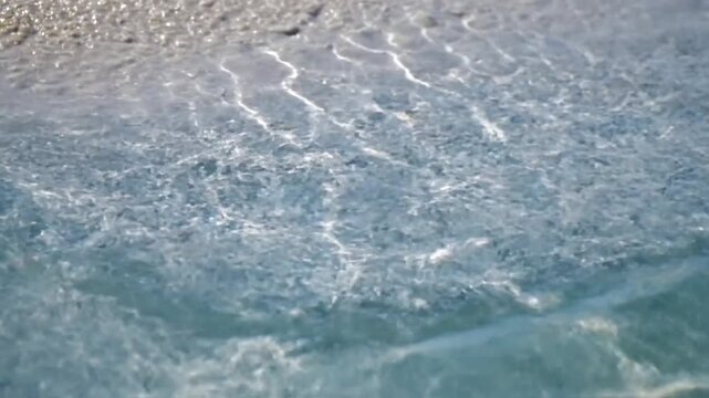 Gentle waves lapping on a sandy beach with sunlight dancing on the water's surface