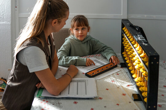 Eight year old girl learning mental arithmetic with abacus under teacher guidance, educational activity and childhood