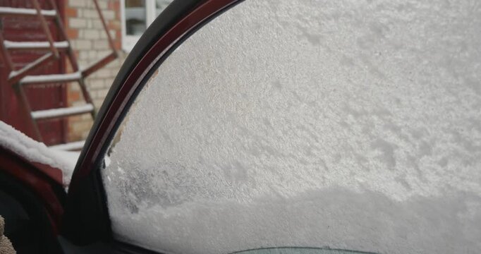 Closeup of a car window covered with frost and ice melting on a cold winter morning as the vehicle's defroster system heats the glass, clearing the view for safe driving.
