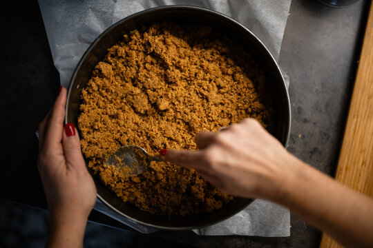 Hands pressing graham cracker crust into springform pan