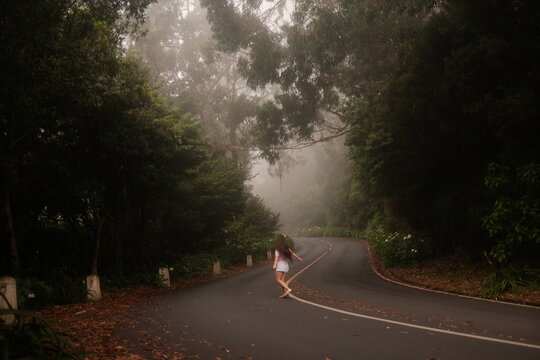 A young woman with long brown hair running on winding forest road in misty morning light, wide shot with copy space for text