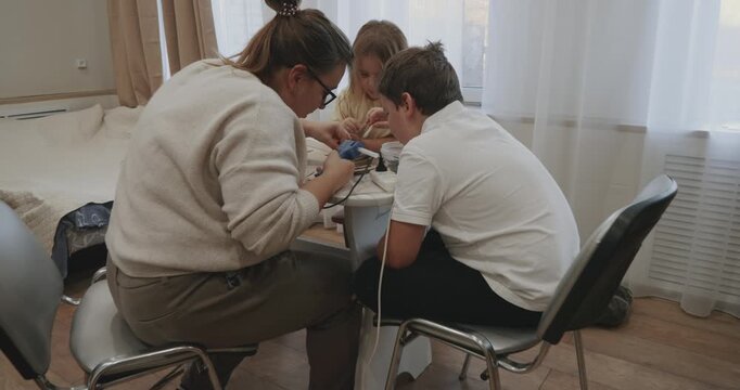 Happy family doing a creative art project. A mother helps her son and daughter use a hot glue gun and natural materials to build a small ship model together at a table at home.