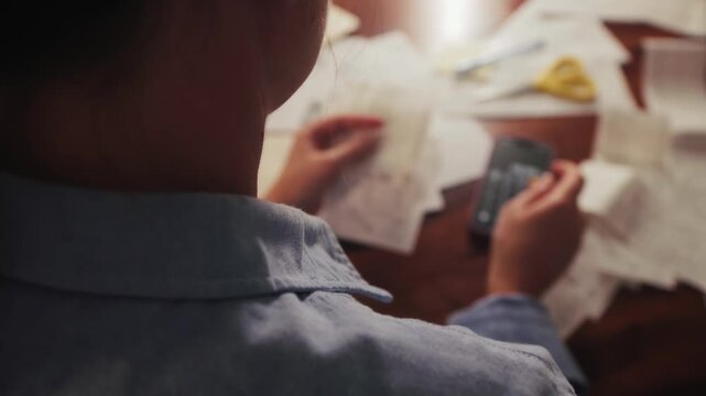 Woman sorts receipts using a calculator to track monthly expenses. Budget planning or tax return from home.