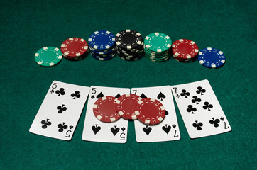 Five playing cards and several stacks of poker chips are on a green table. Friends enjoy a game at night while engaging in a fun activity