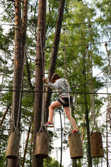 Obraz premium Active Boy Overcoming Rope Course Obstacles in Adventure Park