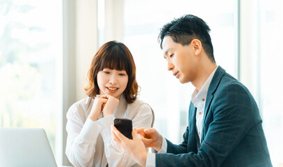Obraz premium スマートフォン画面を確認する上司と部下の打ち合わせシーン, Manager and junior staff checking a smartphone together in office